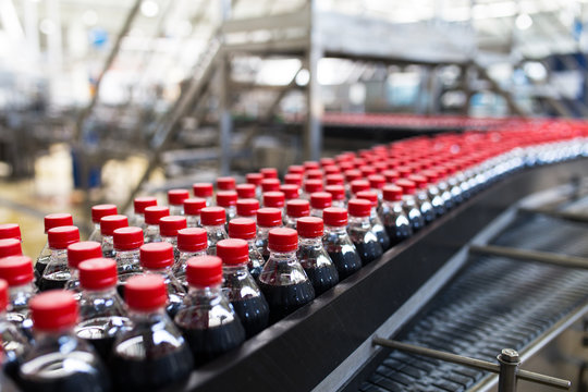Bottling factory - Black juice or soft drink bottling line for processing and bottling juice into bottles. Selective focus. 