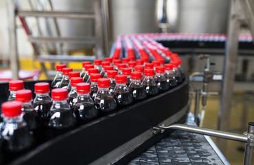 Bottling factory - Black juice or soft drink bottling line for processing and bottling juice into bottles. Selective focus. 