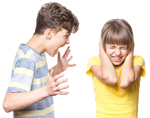 Emotional portrait of brother and sister, quarreling children - teen boy shouting at little girl. Negative human face expression. Conflict concept.