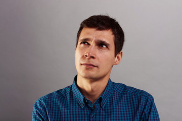 Obraz premium Thoughts, problem-solving and ideas. Close up shot of handsome pensive doubtful adult male with dark hair looking up while trying to find solution to business problem, posing at grey studio wall