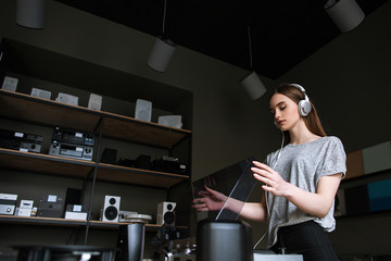 Young lady in music shop choosing vinyl records. Retro audio listening in headphones, modern...