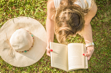 Linda mulher lendo um livro no gramado verde, sol de verão.