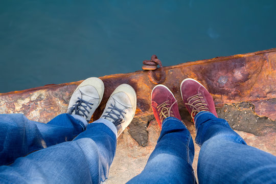A guy with a girl in jeans and keds stands on the edge of a rusty pier.