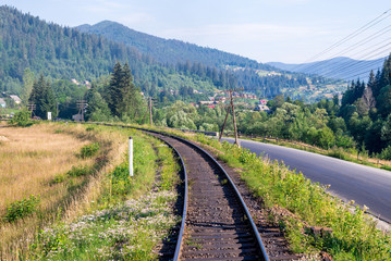 Fototapeta premium Travel, rest. A view of the railway tracks surrounded by trees, grass and bushes. Horizontal frame