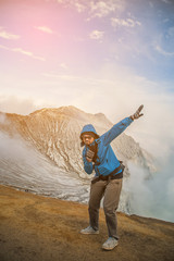 Male photographer with backpack standing on top of a mountain and enjoying sunrise, Colorful Kawah Ijen volcano