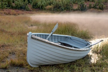 White rowboat on bank of lake on a misty morning 