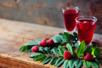Raspberry fruit liqueur in two shot glasses with berries and green leaves