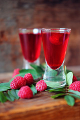 Raspberry fruit liqueur in two shot glasses with berries and green leaves