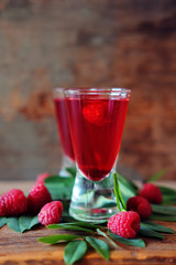 Raspberry fruit liqueur in two shot glasses with berries and green leaves