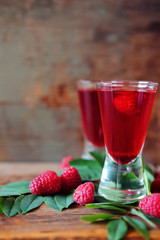 Raspberry fruit liqueur in two shot glasses with berries and green leaves
