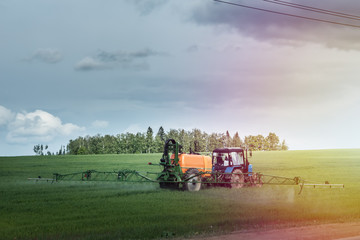 Fototapeta premium Farm machinery spraying insecticide to the green field, agricultural natural seasonal spring background