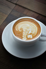 Latte or cappuccino coffee with heart shape in white cup on brown wooden background