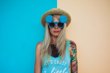 Beautiful young woman hipster with a tattoo in sunglasses and a hat on a bright coloured background. Beach style