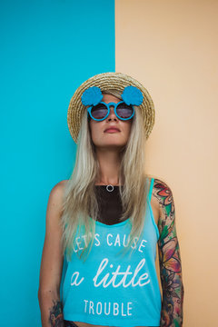 Beautiful young woman hipster with a tattoo in sunglasses and a hat on a bright coloured background. Beach style