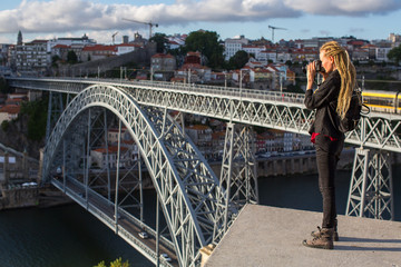 Young woman with dreadlocks takes pictures on the viewing platform opposite the Dom Luis I bridge across the Douro river in Porto, Portugal.