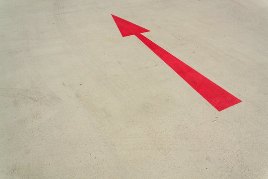 Red arrow direction sign on gray concrete road sunny day