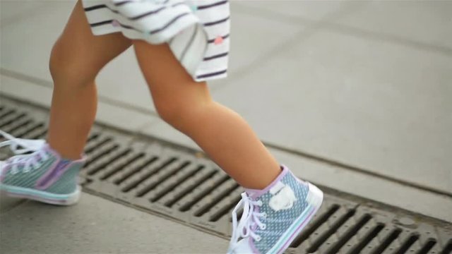 Little Blonde Girl in Dress and Blue Sneakers is Running to Her Mother Wearing Red Shoes. View of the Foots.