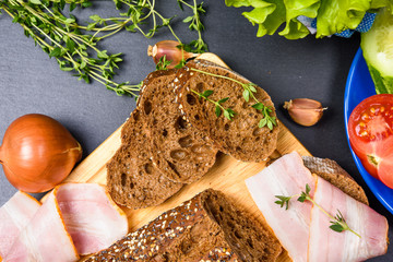 Top view of bread slices on wooden chopping board with herbs, ham and vegetables