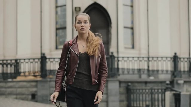 Autumn is coming. Woman in burgundy leather jacket walk in city street, slowmotion.