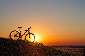 Silhouette of a bike on the hills at sunset.