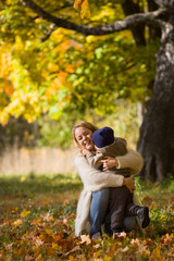 Happy young woman with cute little toddler boy throwing maple leaves and having fun. Mother with child walking in the park and enjoying sunny weather. Lifestyle, family and autumn concept