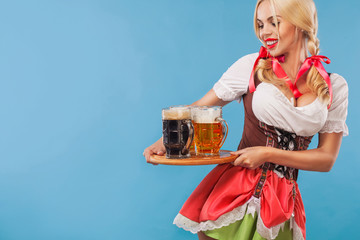 Young sexy Oktoberfest girl - waitress, wearing a traditional Bavarian dress, serving big beer mugs...