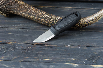 Small tourist knife on a black wooden background with a reindeer horn.