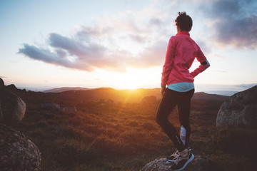 Athletic girl resting after training on running in the mountains at sunset. Sport tight clothes.