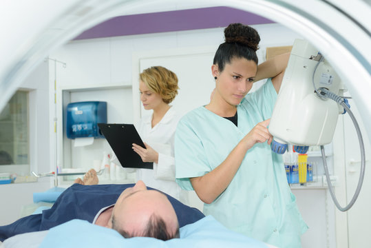 radiologic technician and nurse preparing mri for male patient