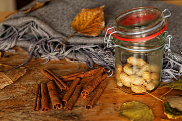 Cinnamon sticks, glass of peanuts, autumn leaves and blanket on a wooden table