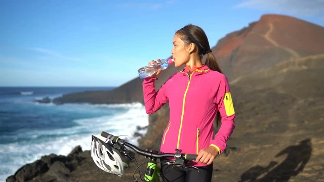 Mountain biking MTB woman drinking water resting from cycling on bike trail. Female mountain biker on bike riding bicycle enjoying healthy active lifestyle in nature.