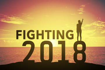 Silhouette young woman standing and raising up her hand about fighting concept on at 2018 over a beautiful sunset or sunrise at the sea. background forhappy new years. success in 2018 years