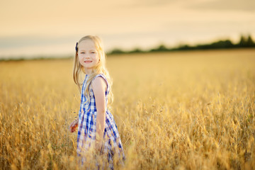 Adorable girl walking happily in wheat field on warm and sunny summer evening