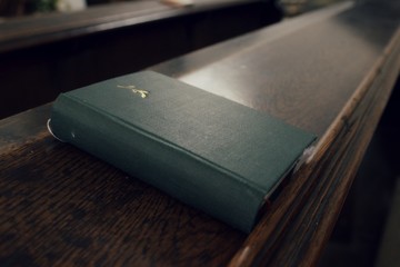Holly bible placed on a church pew. Christian scripture on a wooden bench. Green ancient closed...