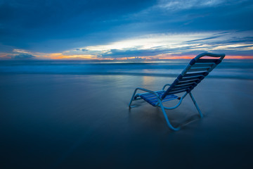 relaxing morning beach chair dramatic early sunrise color sky ocean surf water reflection scene solitude luxury resort vacation