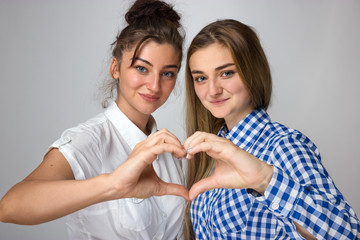 Two young sisters making heart with fingers.