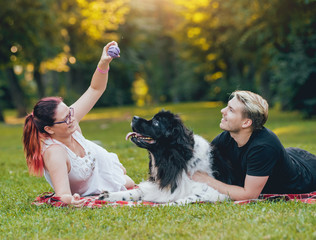 Newfoundland dog plays with man and woman in the park