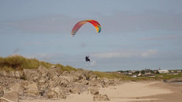 Para-glider flies close to low rocks at the beach
