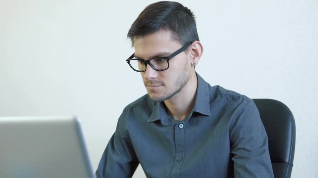 Portrait of a young man wearing glasses sitting in his office in front of a monitor - working on a computer. People stock footage slider shot. 