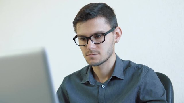 Close-up portrait of a young man wearing glasses sitting in his office in front of a monitor - having a video chat. People stock footage slider shot. 