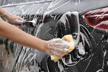 Asian hand holds sponge with car wash To clear the sides of the black car.