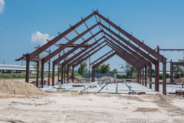 Steel structure of new industrial building under cloud blue sky. New technology structural frame beam of factory in construction. Steel frame manufacturer and pile of sand and gravel in Crosby, TX, US