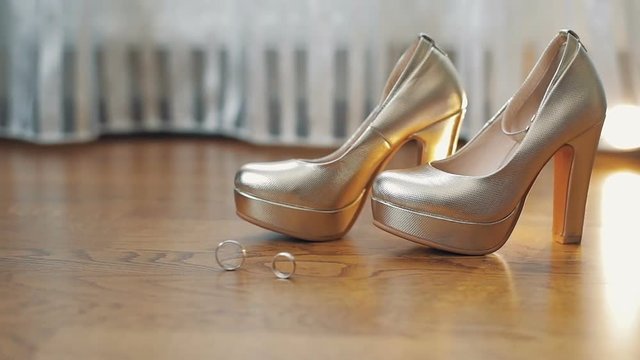 Two wedding rings rolling to each other near bride's wedding shoes