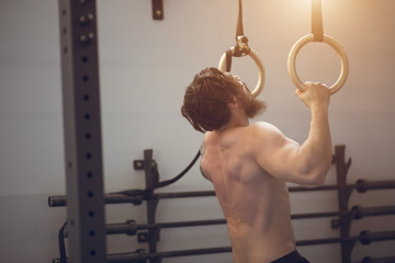 Muscle-up exercise young man doing intense cross fit workout at the gym on gymnastic rings
