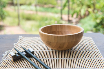 Wooden bowl with chopsticks on bamboo mat  on wooden table in the garden.