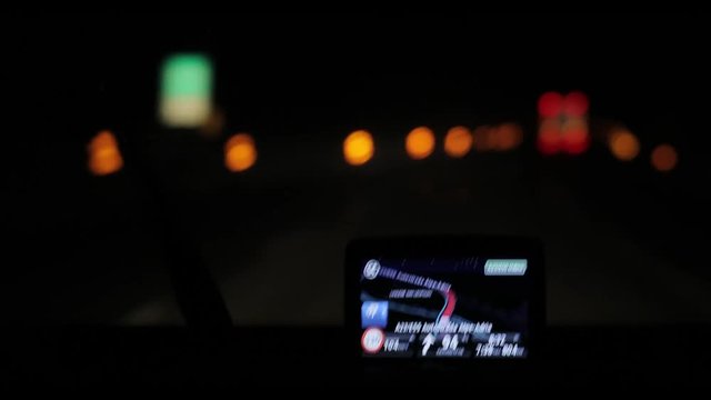 GPS navigation in car driving at night at blurry lights background 4k pov following ambulance or truck. Close-up on navigator screen showing road and speed limit on highway - shaking shot shallow dof