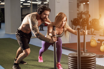 Fitness sled pull with female standing on sled. Two women doing intense physical workout at gym.