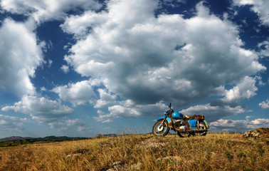 An old motorcycle parked in the field with romantic cloudy sky in the background