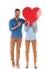 smiling man pointing to the big heart over woman's  face