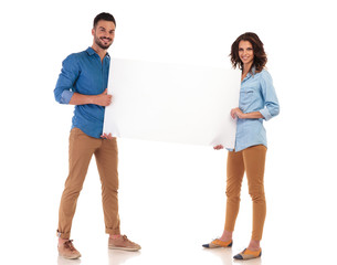 full body picture of smiling young couple holding blank board